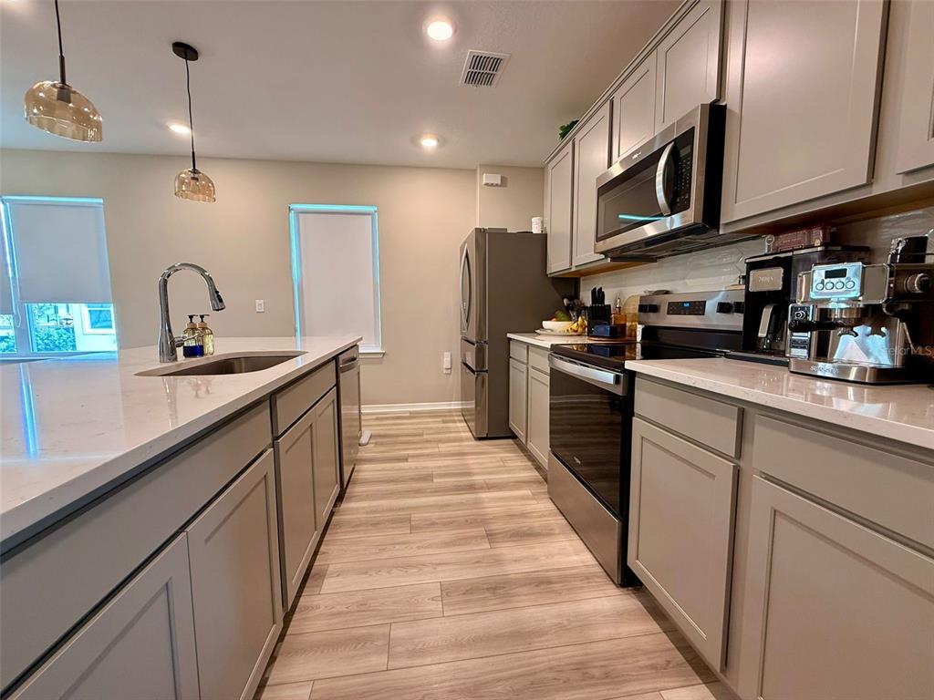A modern kitchen features gray cabinets, white countertops, stainless steel appliances, and wood-look flooring — 6475 BREEZE FILLED LANE, WINTER GARDEN, FL