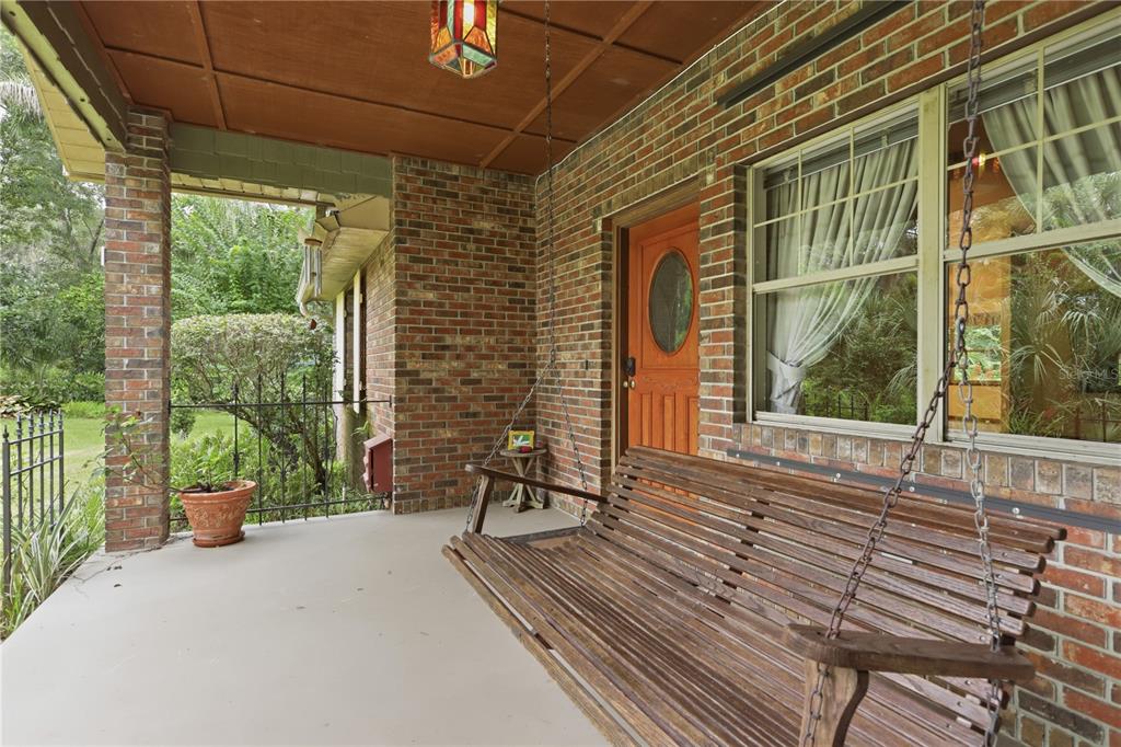 A covered brick porch features a wooden hanging swing, a stained-glass light, and a door — 1925 LADY BUG LANE, DELAND, FL