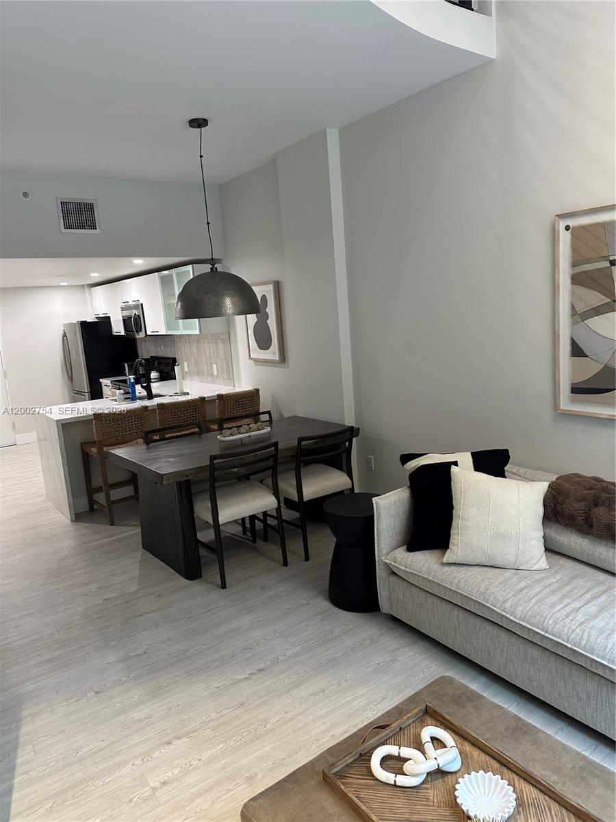 An open-concept living and dining area features a modern kitchen, wooden table, and neutral sofa — 3339 Virginia St # 127, Miami FL 33133, MIAMI, FL