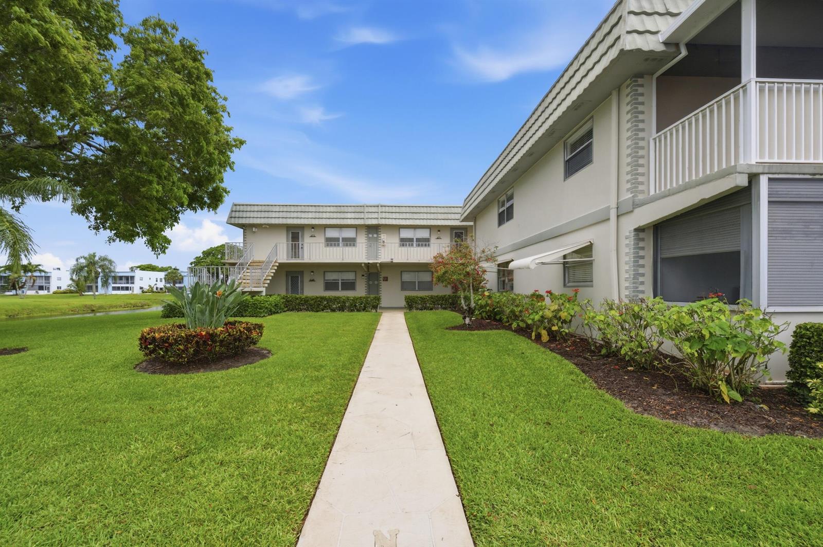 A concrete walkway leads to the entrance of a two-story apartment building with landscaping — 670 Monaco N, Delray Beach FL 33446, DELRAY BEACH, FL