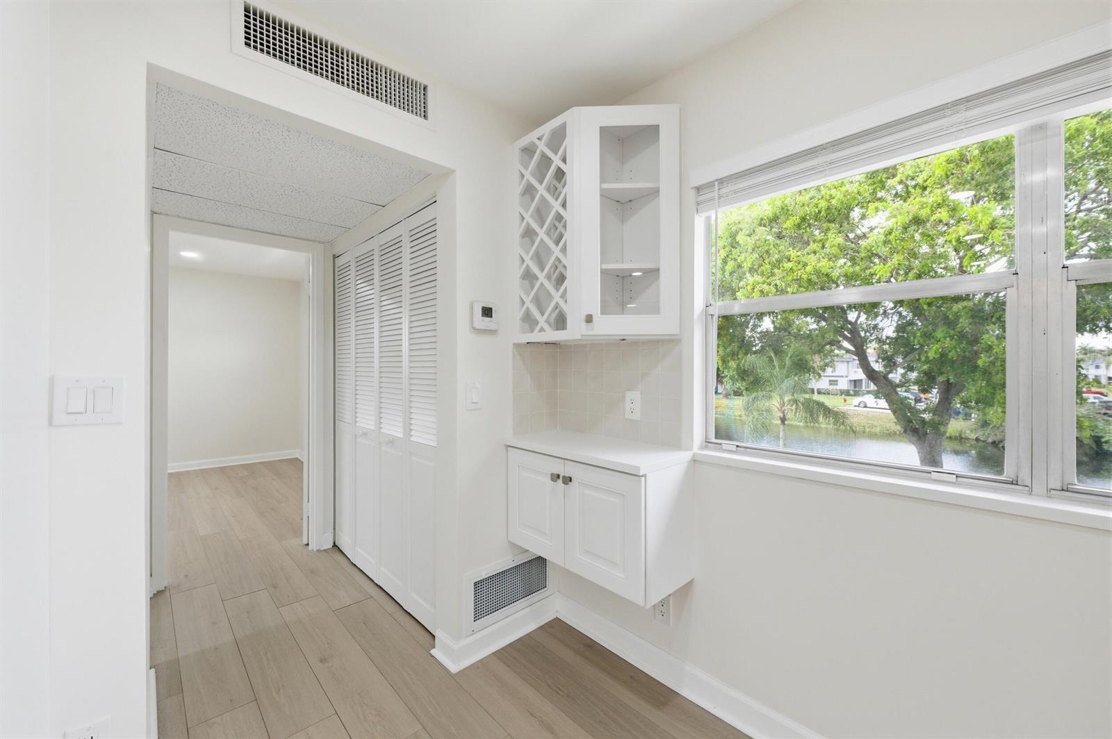 A white built-in cabinet with wine storage sits beside a window overlooking a pond — 670 Monaco N, Delray Beach FL 33446, DELRAY BEACH, FL