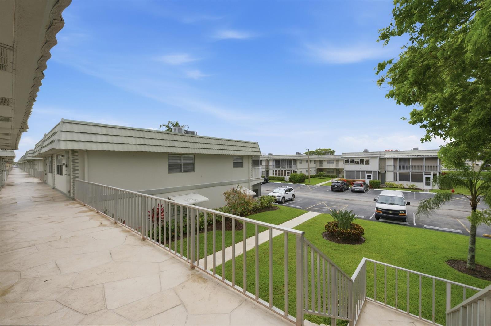 An elevated walkway overlooks a parking lot and apartment buildings on a sunny day — 670 Monaco N, Delray Beach FL 33446, DELRAY BEACH, FL