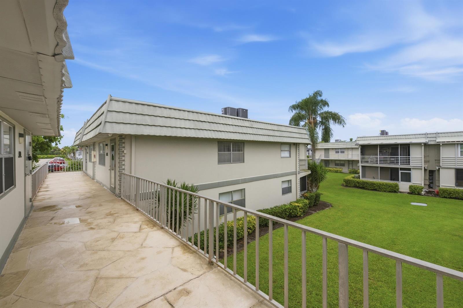 An exterior view of a second-story walkway overlooking a grassy courtyard between apartment buildings — 670 Monaco N, Delray Beach FL 33446, DELRAY BEACH, FL