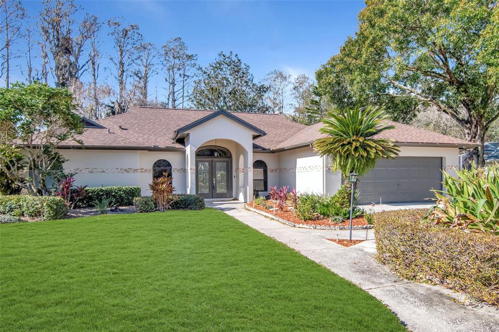 A single-story house with a beige stucco exterior, a brown shingled roof, and a front lawn — 18306 PLEASANT RIDGE PLACE, LUTZ, FL