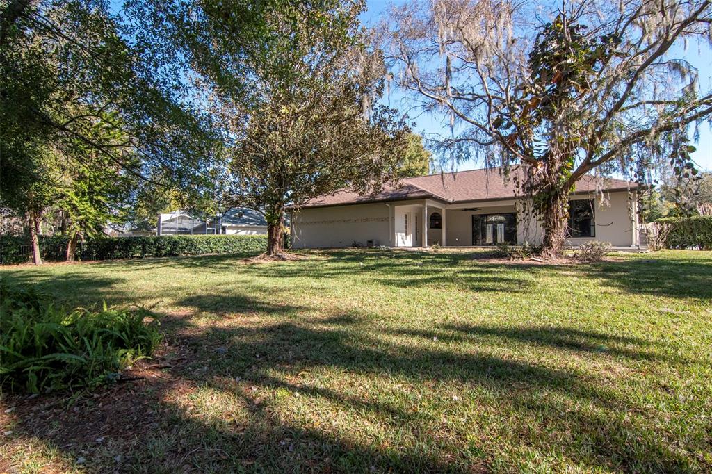 A single-story house with a brown roof sits behind a large, grassy backyard with trees — 18306 PLEASANT RIDGE PLACE, LUTZ, FL