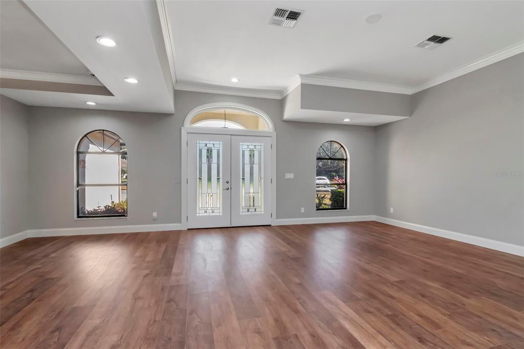 A spacious room with light gray walls, wood-look flooring, and a double-door entryway — 18306 PLEASANT RIDGE PLACE, LUTZ, FL