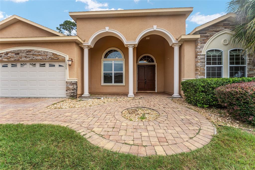 The exterior of a tan stucco house features a stone-accented garage and arched entryway — 14540 NW 27TH PLACE, NEWBERRY, FL
