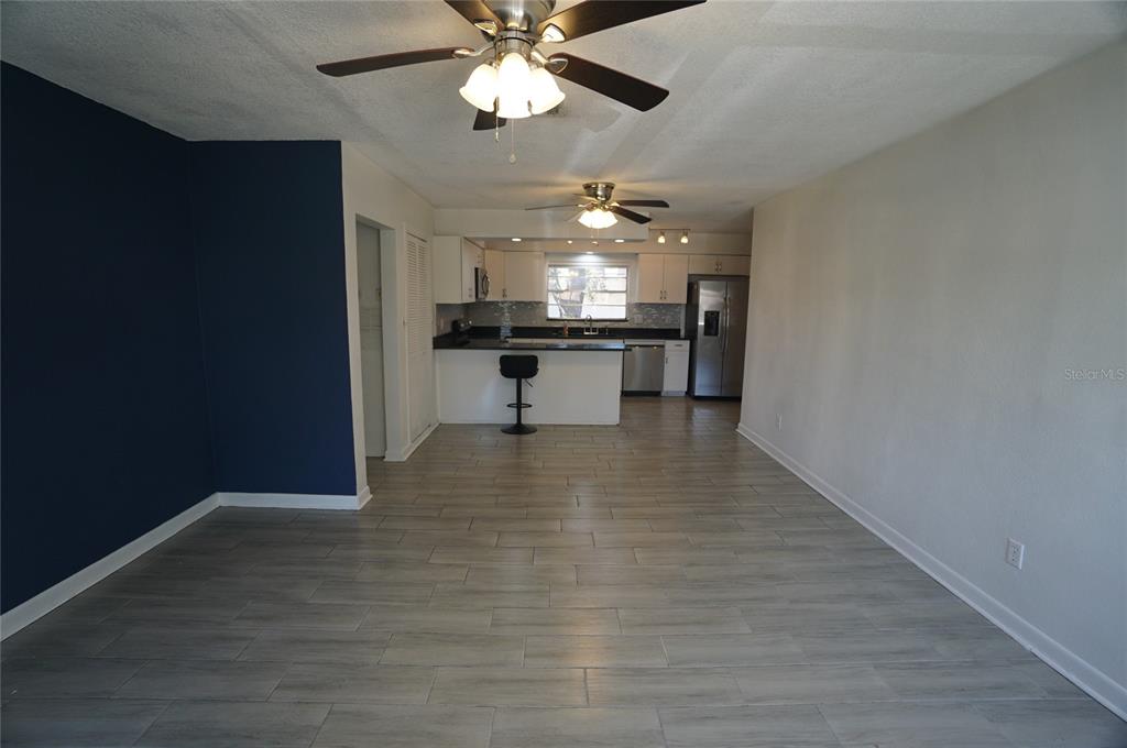 An open-concept living area with gray tile flooring leads to a kitchen with white cabinets — 3916 W NORTH A STREET, TAMPA, FL