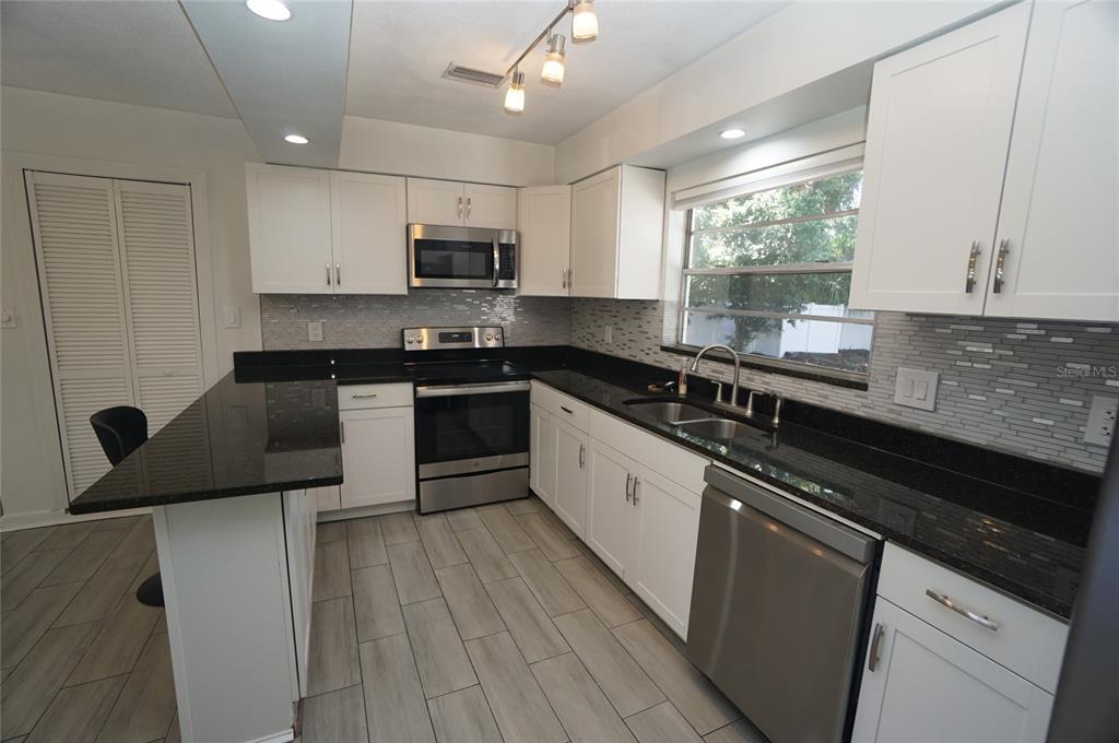 A kitchen features white cabinets, black countertops, stainless steel appliances, and light wood-look tile flooring — 3916 W NORTH A STREET, TAMPA, FL