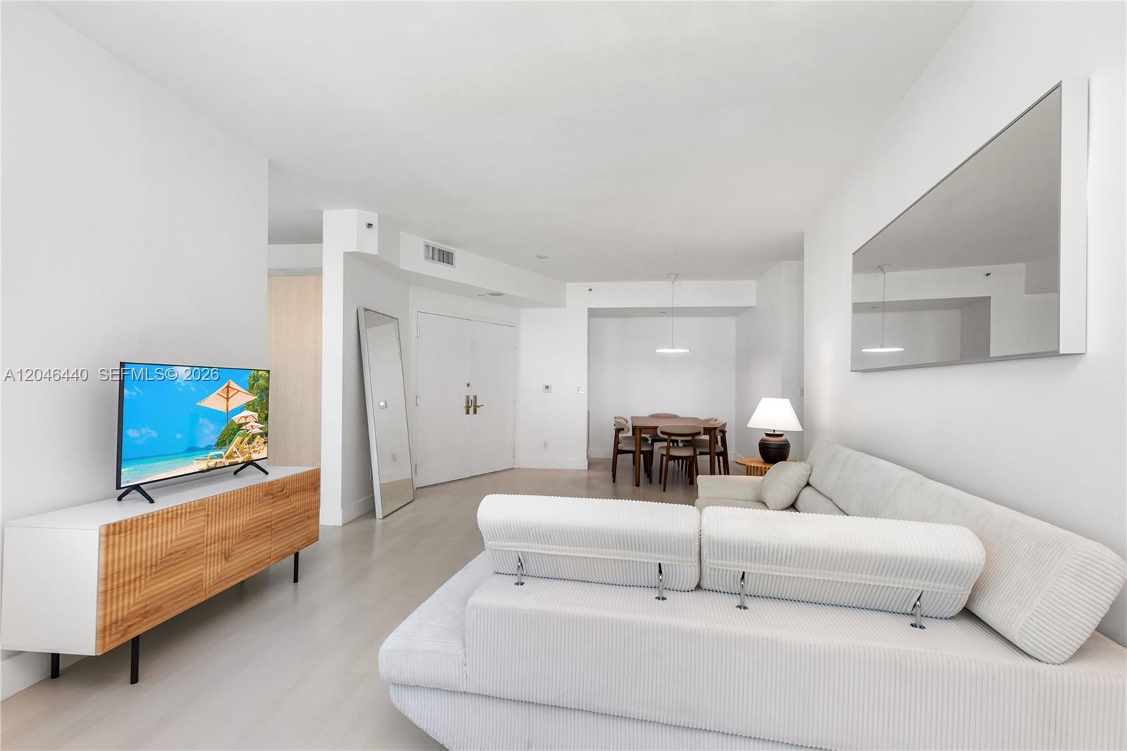 A living room features a white sofa, a wooden media console, and a dining area — 300 S Pointe Dr # 907, Miami Beach FL 33139, MIAMI BEACH, FL
