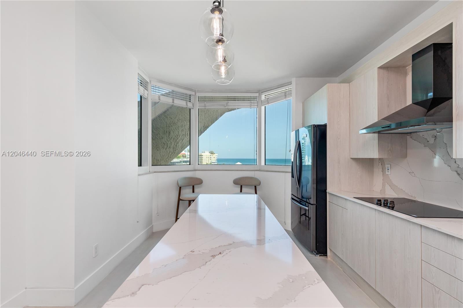 A modern kitchen features a long marble island, light wood cabinetry, and ocean views — 300 S Pointe Dr # 907, Miami Beach FL 33139, MIAMI BEACH, FL
