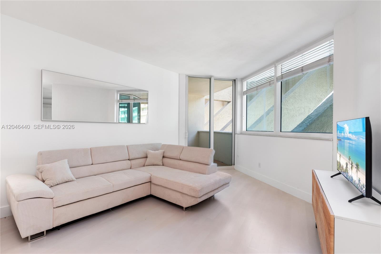 A living room features a beige sectional sofa, a television, and a balcony door — 300 S Pointe Dr # 907, Miami Beach FL 33139, MIAMI BEACH, FL