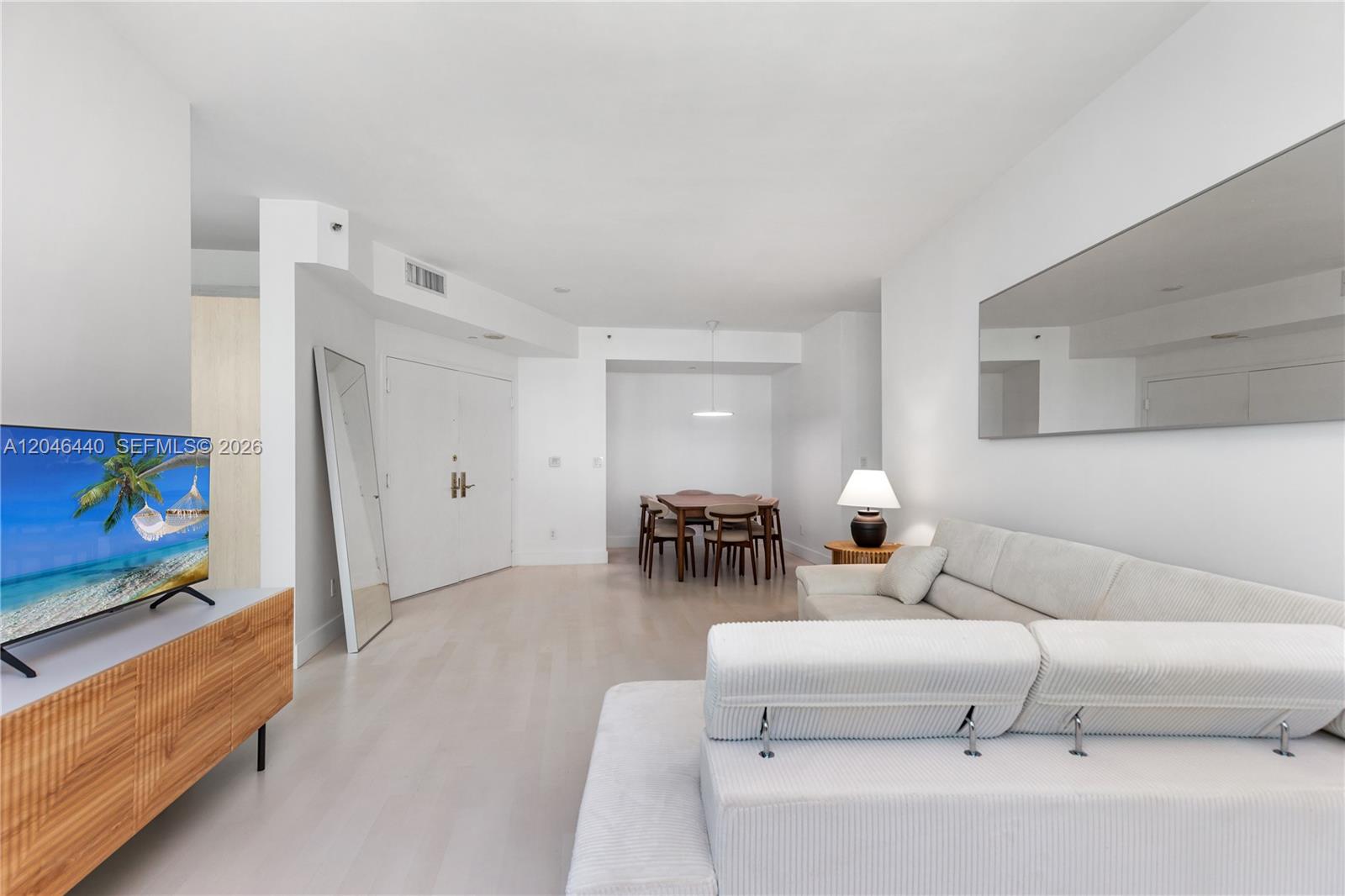 A bright living and dining area features white walls, light wood flooring, and modern furniture — 300 S Pointe Dr # 907, Miami Beach FL 33139, MIAMI BEACH, FL