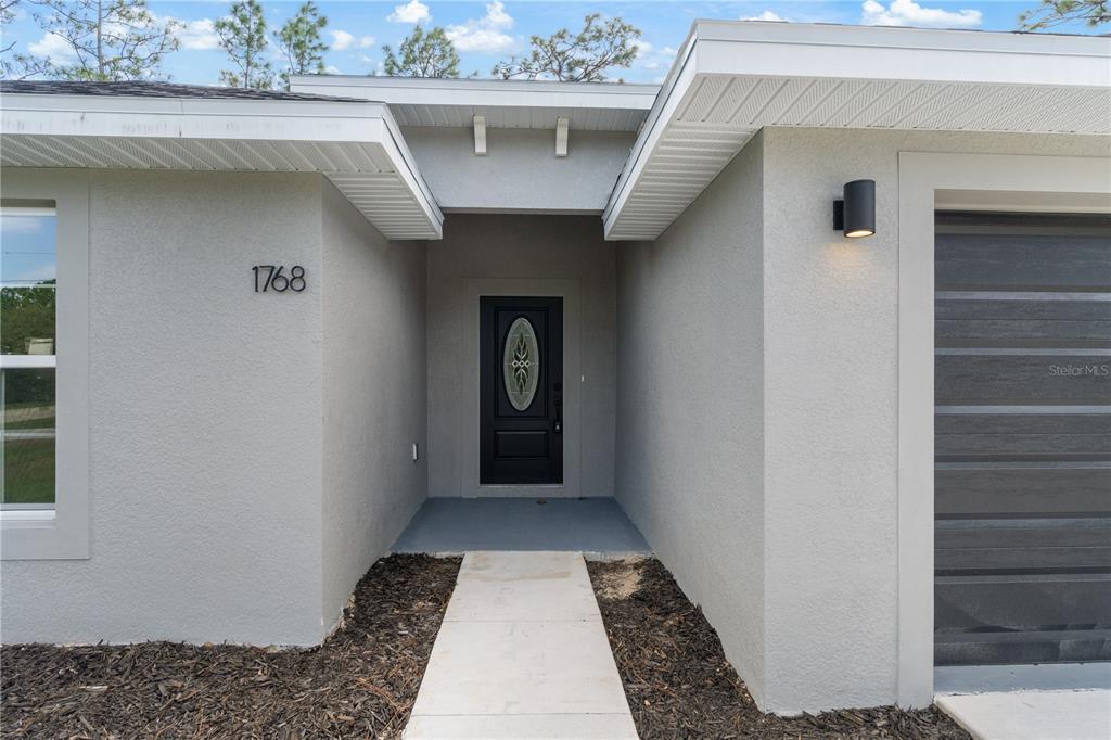 The exterior of a house features a gray stucco facade, a black front door, and a walkway — 1768 E BISMARK ST, HERNANDO, FL