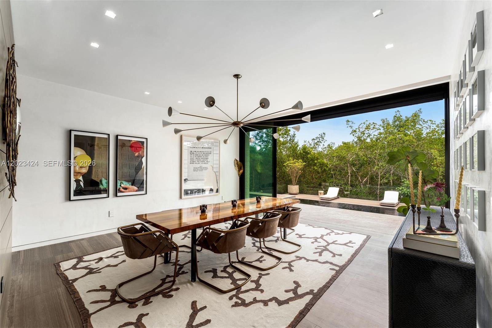 A modern dining room features a wooden table, leather chairs, and a large sliding glass wall — 132 Paloma Dr, Coral Gables FL 33143, CORAL GABLES, FL