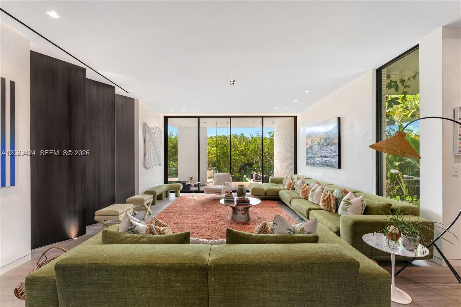 A spacious living room features a large green sectional sofa, an orange rug, and floor-to-ceiling windows — 132 Paloma Dr, Coral Gables FL 33143, CORAL GABLES, FL