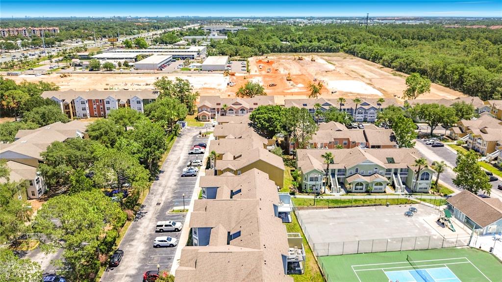 An aerial view shows apartment buildings, a parking lot, a tennis court, and construction land — 8716 RAIN FOREST PLACE UNIT A, KISSIMMEE, FL