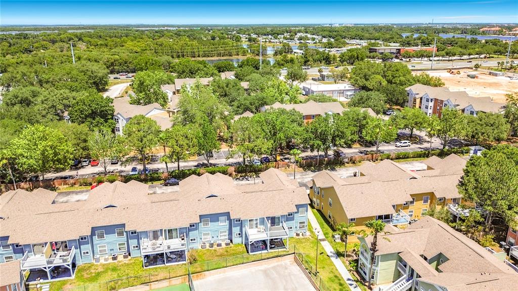 An aerial view shows multiple apartment buildings with brown roofs and a tennis court — 8716 RAIN FOREST PLACE UNIT A, KISSIMMEE, FL