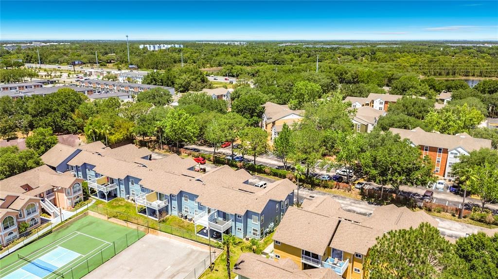 An aerial view shows multi-story apartment buildings, a tennis court, and surrounding trees — 8716 RAIN FOREST PLACE UNIT A, KISSIMMEE, FL
