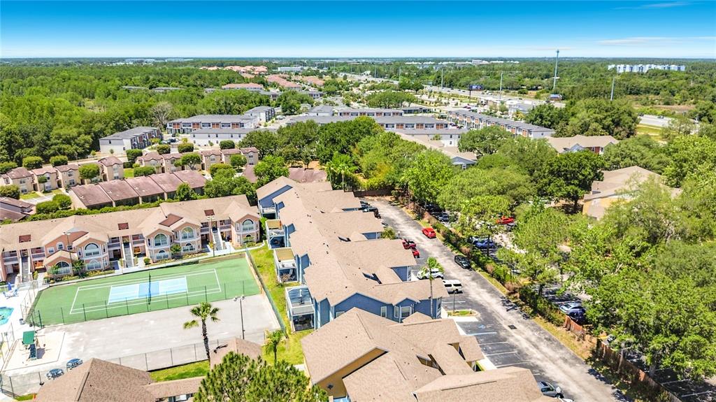 An aerial view shows multi-story apartment buildings, a tennis court, and a parking lot — 8716 RAIN FOREST PLACE UNIT A, KISSIMMEE, FL