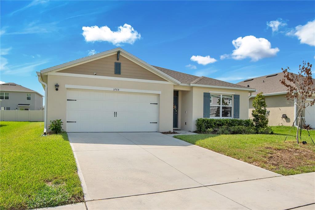 A single-story house with a beige stucco exterior, a two-car garage, and a concrete driveway — 3768 BOTANICAL WAY, SANFORD, FL