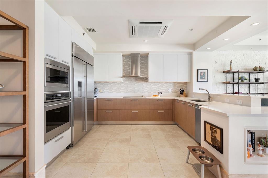 A modern kitchen features white upper cabinets, wood lower cabinets, stainless steel appliances, and tile flooring — 500 PLANTATION DRIVE UNIT 3206, DORADO, PR