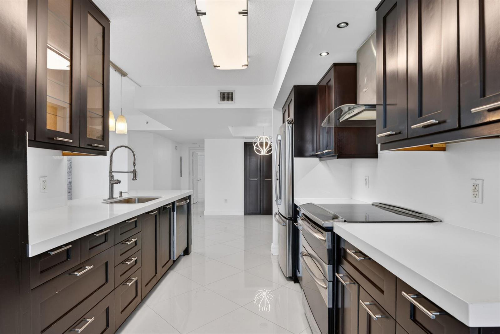 A galley kitchen features dark wood cabinets, white countertops, stainless steel appliances, and tile flooring — 3232 Coral Way # 1601, Miami FL 33145, MIAMI, FL