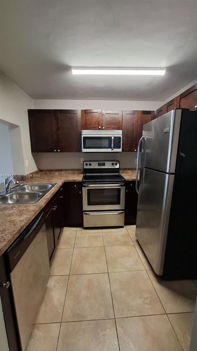 A kitchen features dark wood cabinets, stainless steel appliances, and tan laminate countertops — 496 NW 165th St Rd # 612, Miami FL 33169, MIAMI, FL