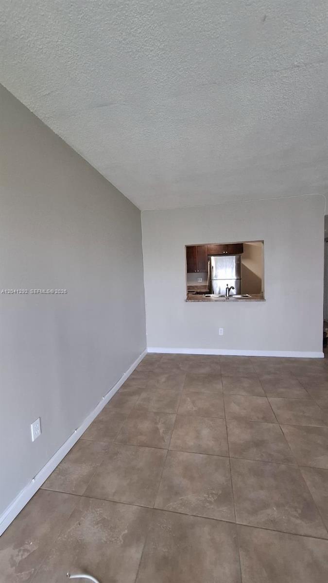 An empty room with light-colored walls and tile flooring features a kitchen pass-through window — 496 NW 165th St Rd # 612, Miami FL 33169, MIAMI, FL