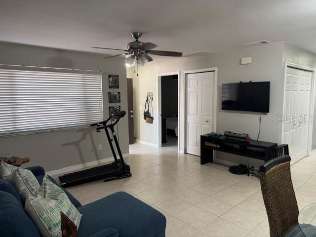 A living room features a treadmill, a blue sofa, a wall-mounted television, and tile flooring — 8472 60TH STREET N, PINELLAS PARK, FL