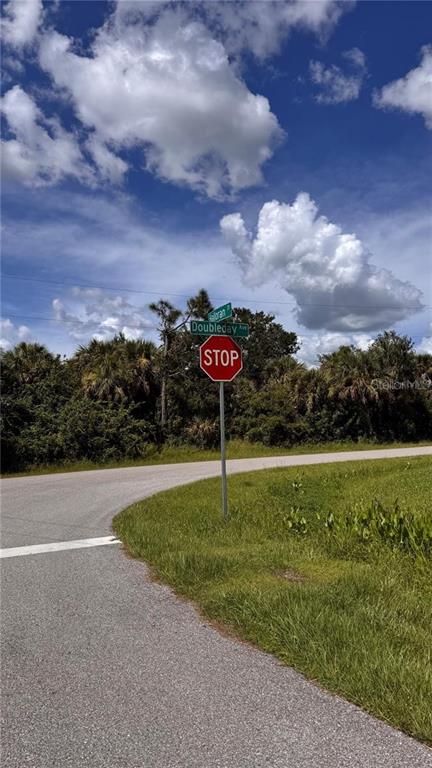 A stop sign stands at a street corner intersection with trees in the background — 13068 DOUBLEDAY AVENUE, PORT CHARLOTTE, FL