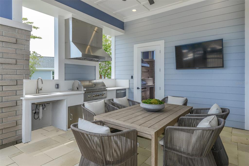 An outdoor kitchen and dining area features a grill, sink, and table on a patio — 7545 LAUREATE BOULEVARD UNIT 7303, ORLANDO, FL