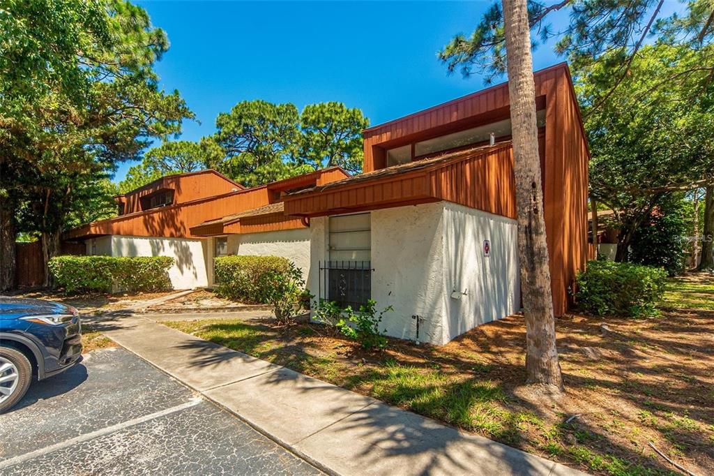 A multi-level townhouse with brown wood siding and white stucco walls under a clear sky — 2064 SUNSET POINT ROAD UNIT 73, CLEARWATER, FL