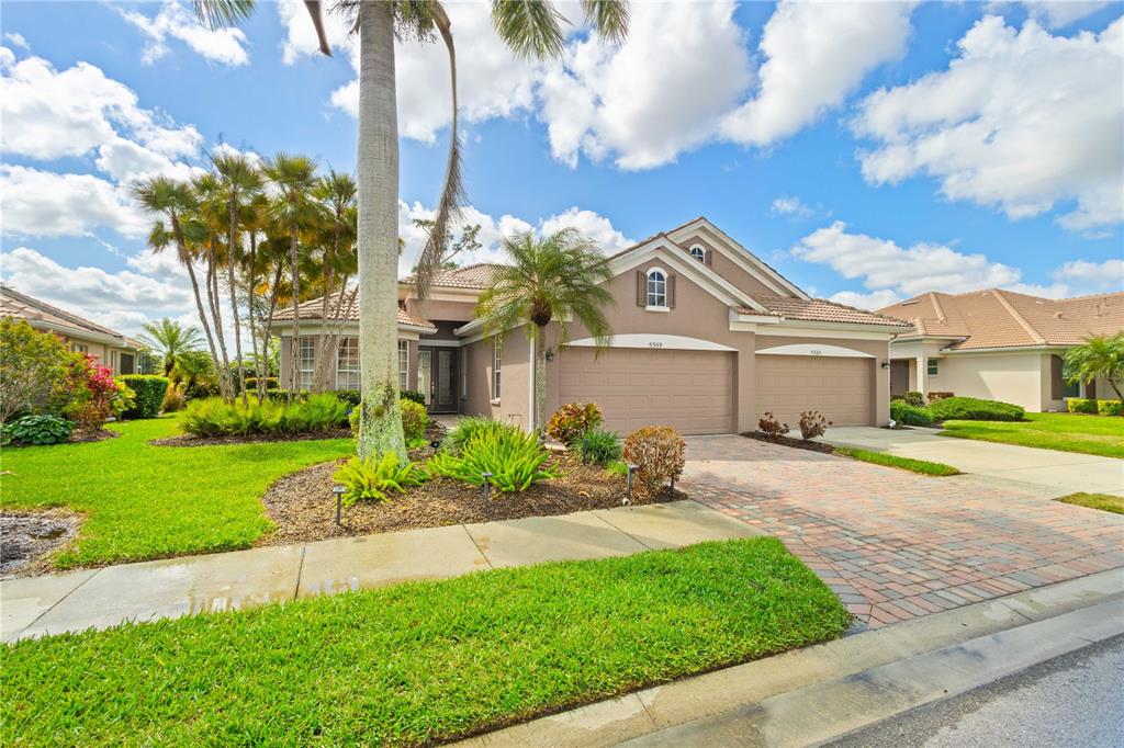 A single-story house with a tan stucco exterior, a three-car garage, and a brick driveway — 5359 WHITE IBIS DRIVE, NORTH PORT, FL