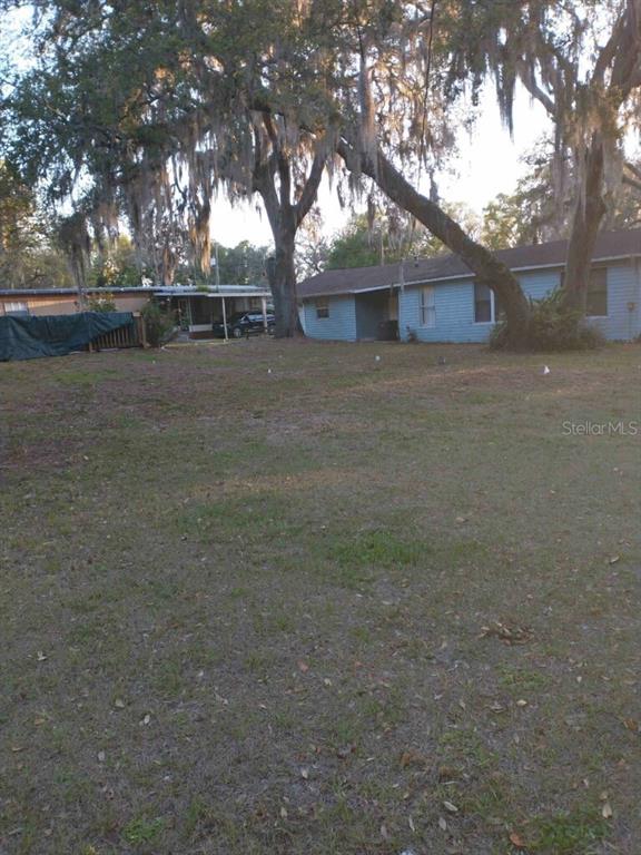 A grassy yard sits in front of a light blue house with large oak trees — 1611 INDIAN TRAIL, LEESBURG, FL