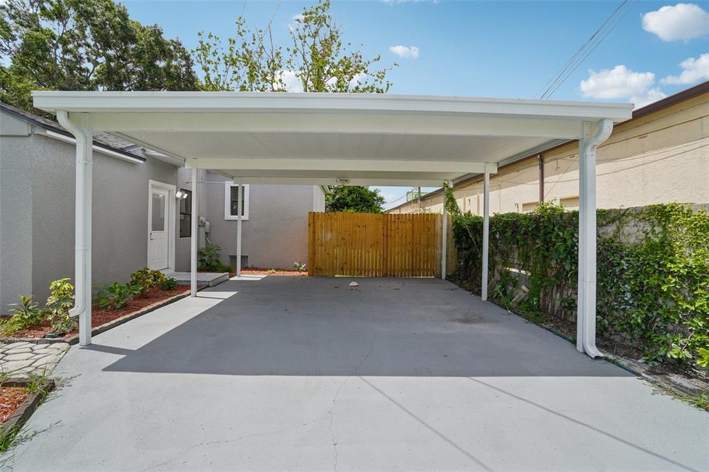 A concrete driveway features a white metal carport structure next to a gray house — 3710 W GRIFLOW STREET, TAMPA, FL