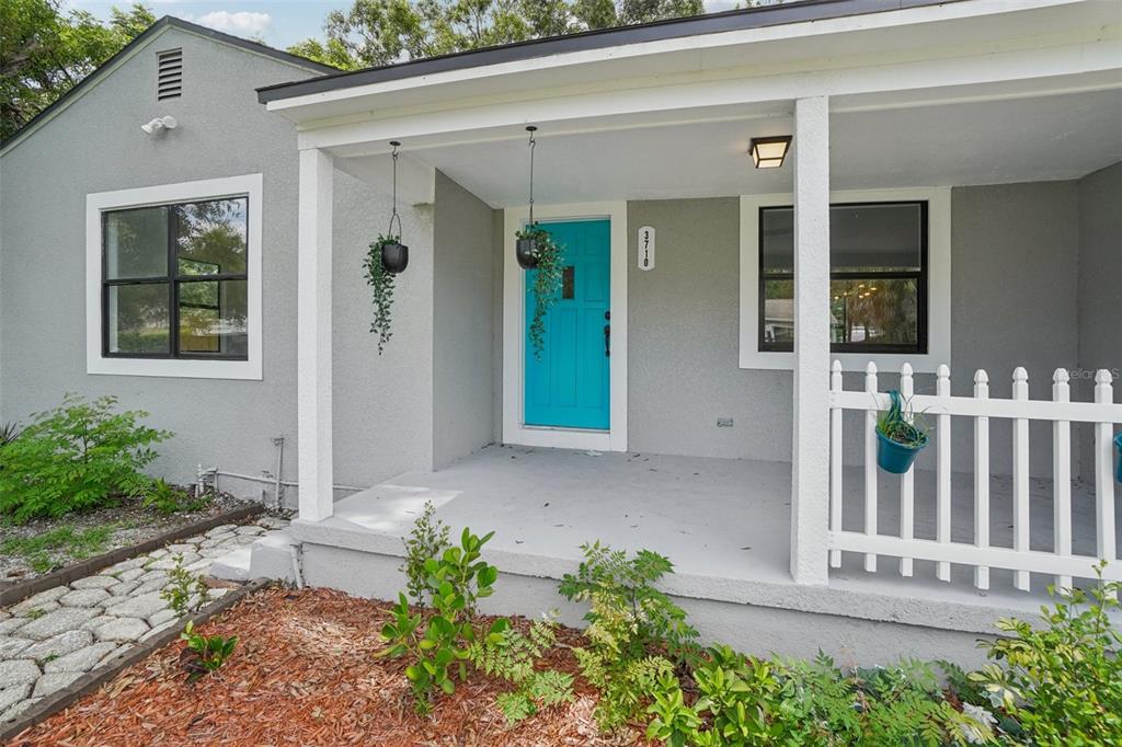 A gray house exterior features a bright blue front door and a white porch railing — 3710 W GRIFLOW STREET, TAMPA, FL