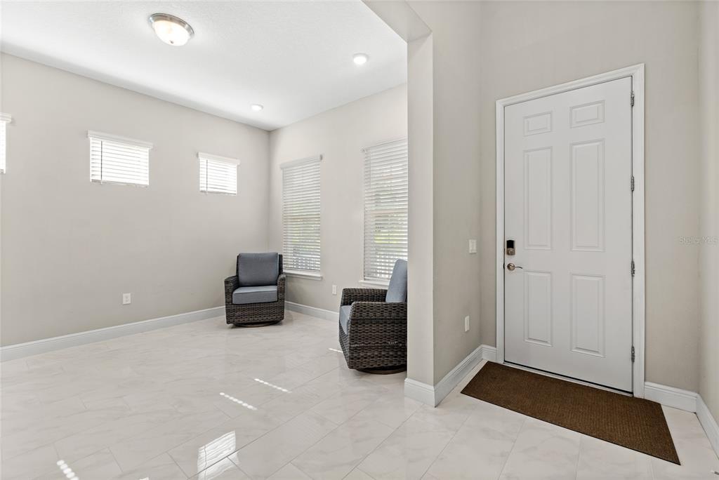 A bright entryway features white tile floors, light gray walls, and two wicker armchairs — 15031 GUAVA BAY DRIVE, WINTER GARDEN, FL
