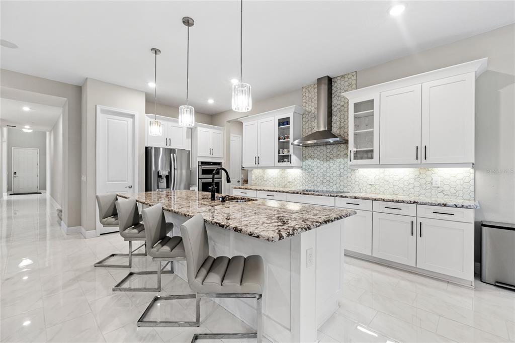 A modern kitchen features white cabinetry, a granite island with bar stools, and stainless appliances — 15031 GUAVA BAY DRIVE, WINTER GARDEN, FL