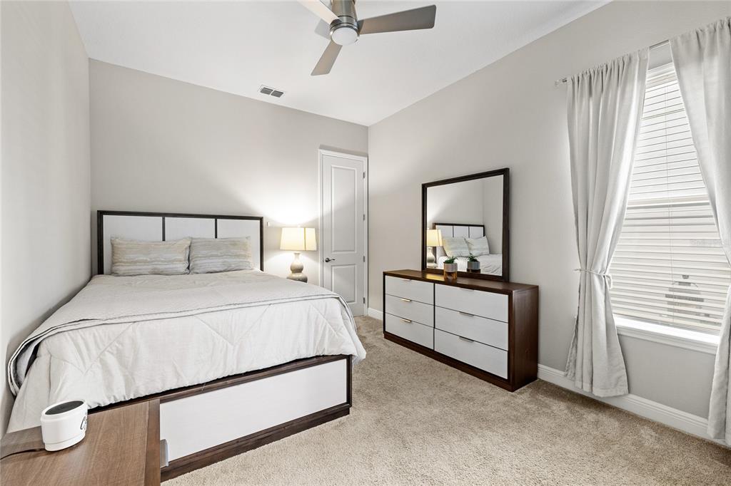 A bedroom features a bed, a dresser with a mirror, and a window with curtains — 15031 GUAVA BAY DRIVE, WINTER GARDEN, FL