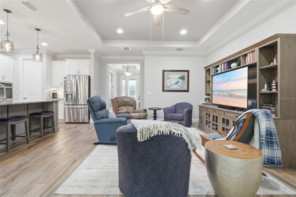 A living room with wood-look flooring, a large entertainment center, and an open-concept kitchen — 103 OLD MOSS CIRCLE, DELAND, FL