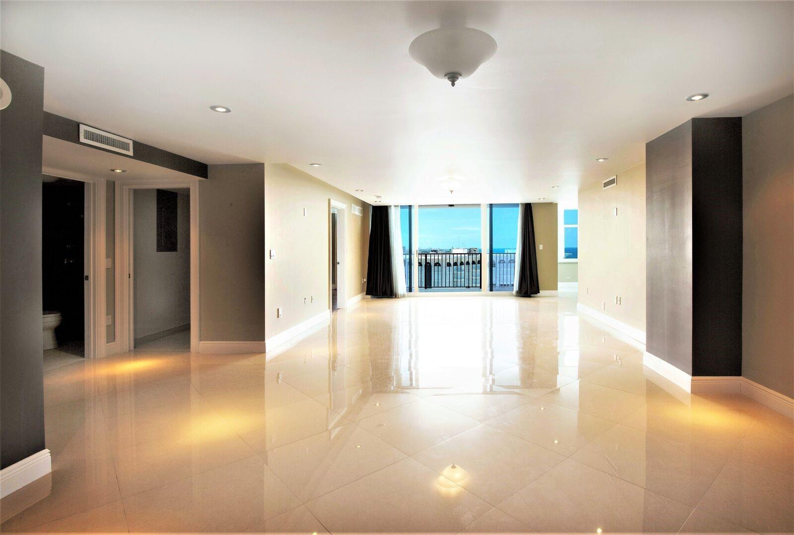 An empty, spacious living room features glossy tile floors, recessed lighting, and a balcony with ocean views — 1360 S Ocean Boulevard # 2806, Pompano Beach FL 33062, POMPANO BEACH, FL