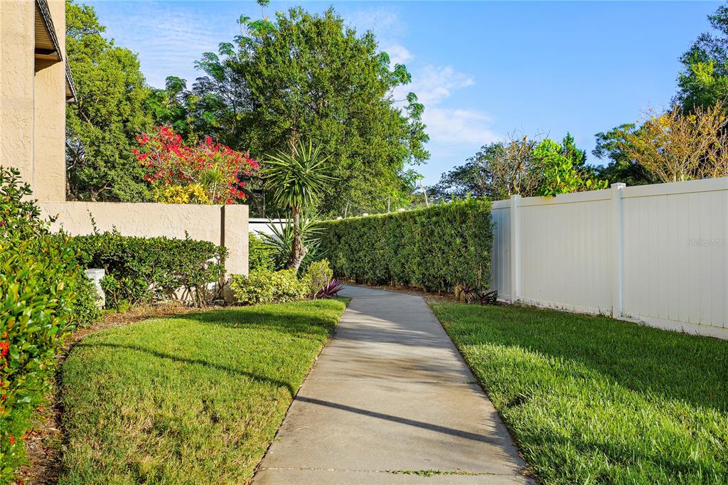 A concrete walkway leads through a grassy yard between a hedge and a white fence — 504 CORDOVA GREEN, SEMINOLE, FL