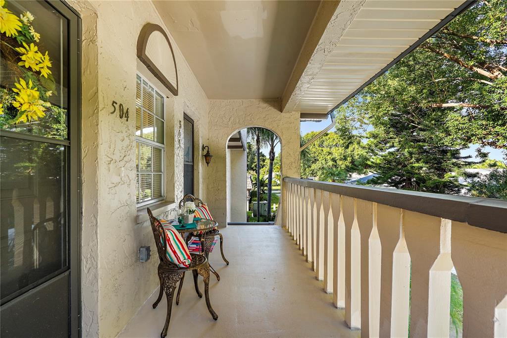 A covered outdoor balcony features a small bistro set, a white railing, and stucco walls — 504 CORDOVA GREEN, SEMINOLE, FL