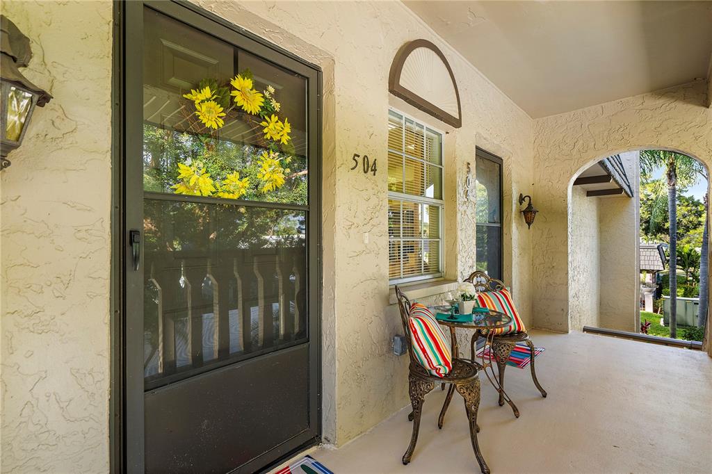 A covered front porch features a screen door, a small bistro set, and stucco walls — 504 CORDOVA GREEN, SEMINOLE, FL