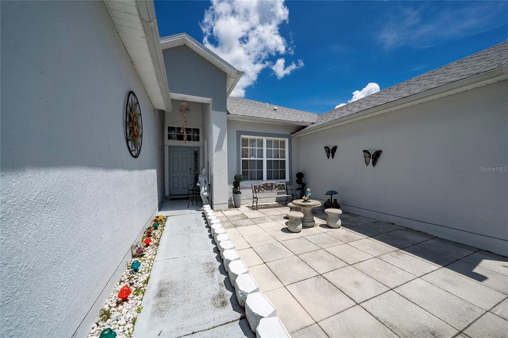 A paved courtyard leads to a front entryway with a white door and stone accents — 661 ELBRIDGE DRIVE, KISSIMMEE, FL