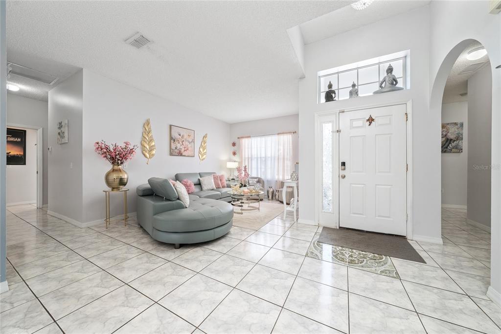 A living room features light tile flooring, a grey sectional sofa, and a white door — 661 ELBRIDGE DRIVE, KISSIMMEE, FL