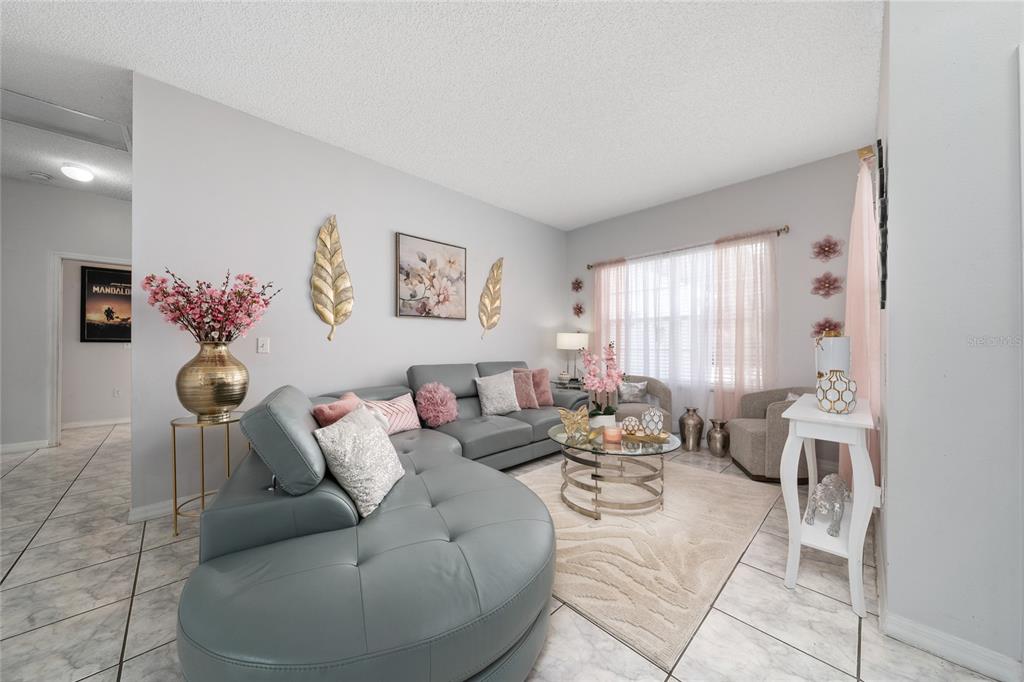 A living room features a grey curved sectional sofa, a glass coffee table, and pink accents — 661 ELBRIDGE DRIVE, KISSIMMEE, FL