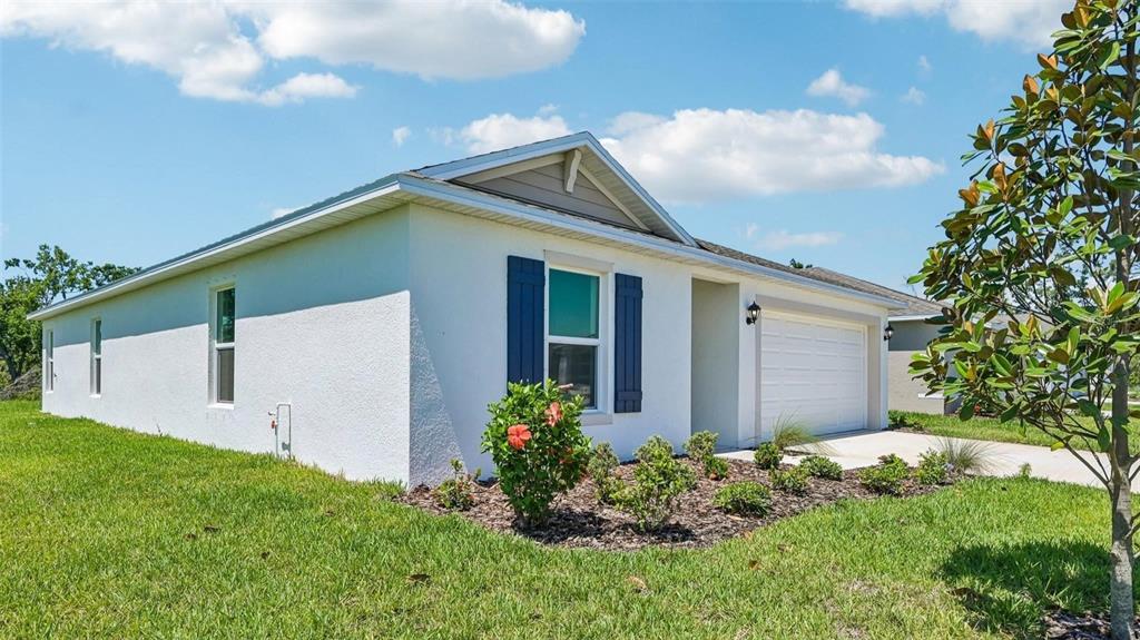 A white single-story house with a two-car garage and blue shutters on a sunny day — 12412 HOPSCOTCH AVENUE E, PALMETTO, FL