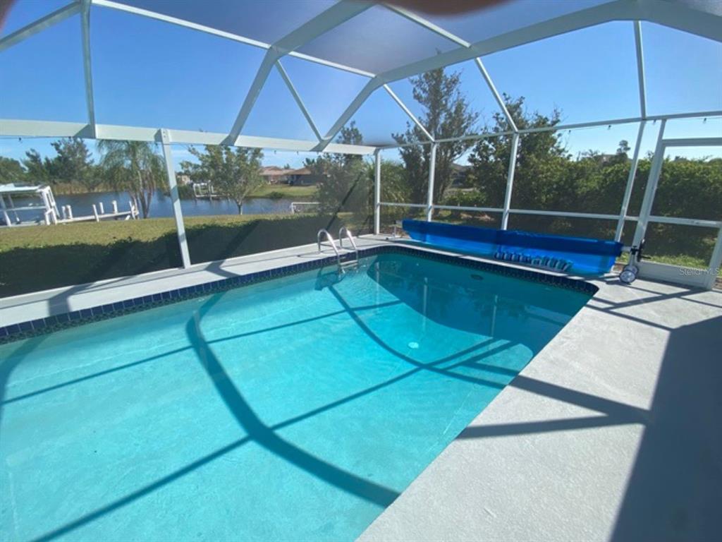 A screened-in swimming pool overlooks a lake with a blue pool cover on the deck — 9500 ATTICA CIRCLE, PORT CHARLOTTE, FL